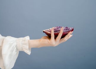 Dieta przeciwzapalna a zdrowie skóry: jak komponować posiłki, które wspierają cerę od wewnątrz Dłoń kobiety trzymająca przekrojoną czerwoną kapustę na niebieskim tle